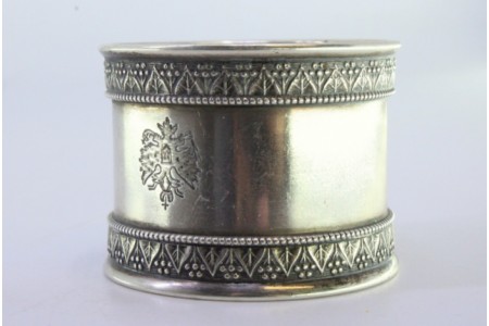 Argola de guardanapo em prata com frisos em relevo e brasão ao centro.